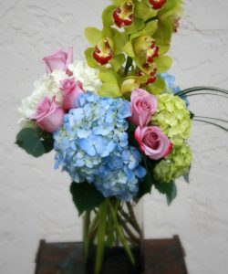 green orchids with blue and pink pastel floral accents in vase