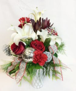 red roses, white lilies, white hydrangea, silver and red accessories arranged around with festive Christmas greens.