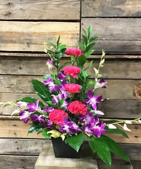 Bursting with happy thoughts this brightly colored arrangement features fresh hot pink carnations and exotic purple orchids in a one sided design. 