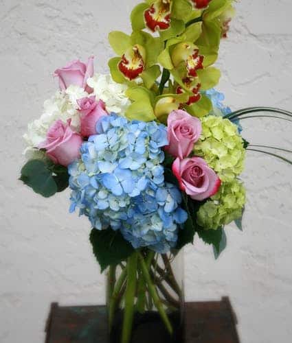 Got someone on your mind? Send this bright display of blue, white and crisp green hydrangea, lavender roses and a cymbidium orchid.